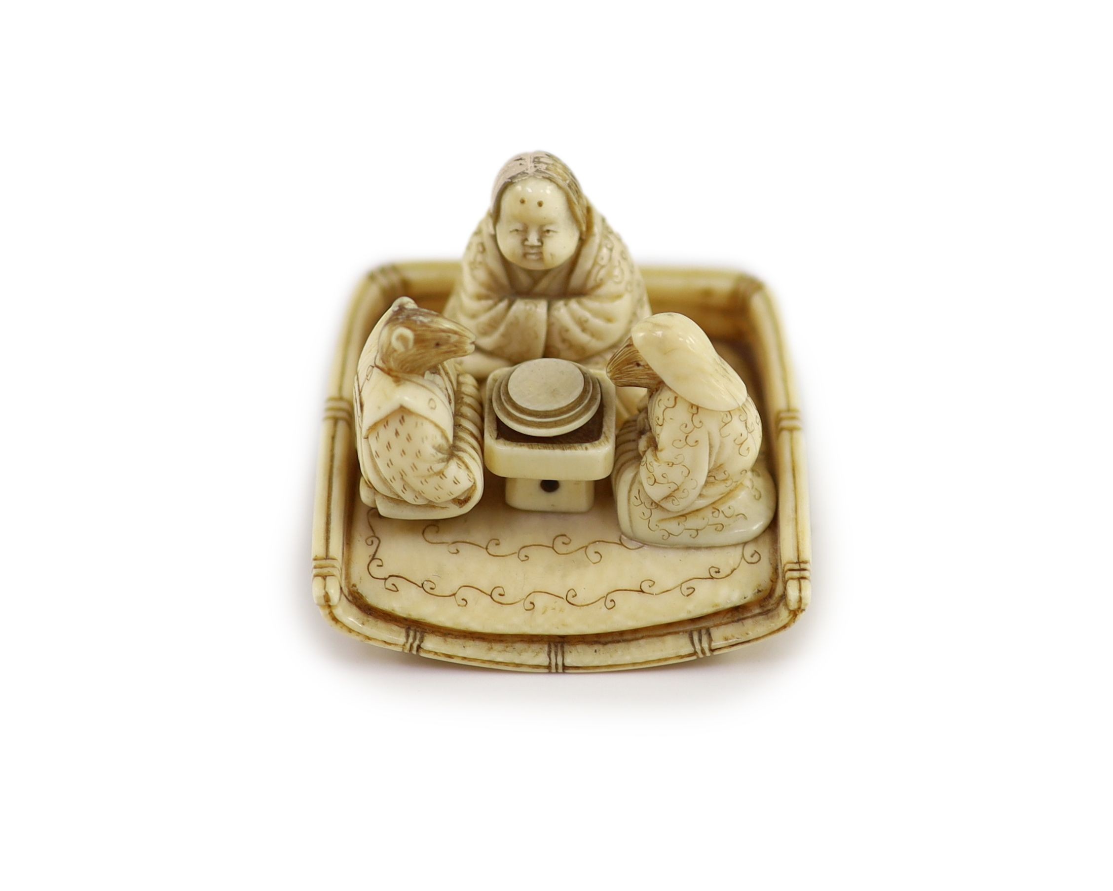 A Japanese ivory netsuke of figures seated around a table, Meiji period, 4.5 cm